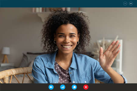 Screen application view of smiling millennial African American woman wave greet talking on video call at home. Happy young biracial female have pleasant webcam digital virtual online conference.の写真素材