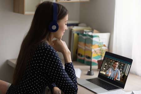 Back view happy young businesswoman involved in online videocall with partner, suing computer application, quarantine lifestyle concept. Smiling employee consulting with company leader distantly.の写真素材