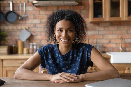 Portrait of smiling African American young woman sit at table at home talk on video call. Happy millennial 20s biracial girl have webcam virtual digital chat or conversation. Communication concept.の写真素材