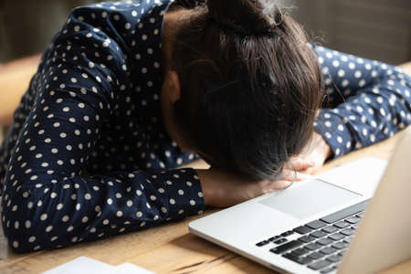 Close up woman sit at desk near laptop put head on hands. Bored office worker falling asleep feels...