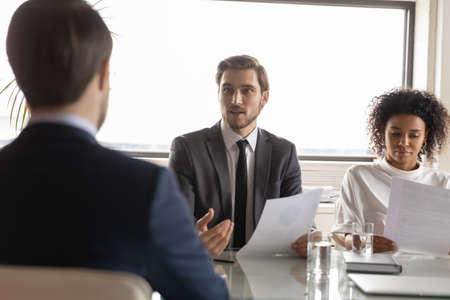 Back rear view confident team leader listening to young male colleague reporting sales or explaining...