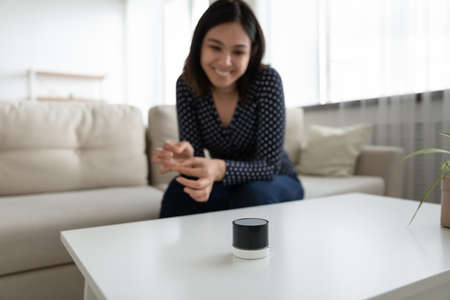 Crop close up of smiling asian girl relax on sofa at home listen to good quality sound music on modern smart wireless speaker. Happy Vietnamese woman client buyer satisfied with mobile audio device.の写真素材