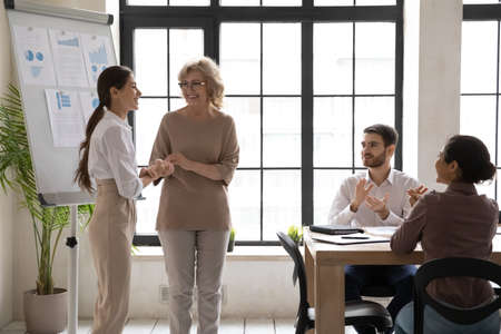 Happy businesswoman handshake greeting new employee or worker at team meeting in office. Smiling diverse businesspeople applaud welcome newcomer newbie to team at briefing. Recruitment concept.の写真素材