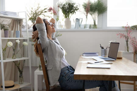 Calm young Caucasian female designer sit lean relax in chair in own atelier or office, relieve...