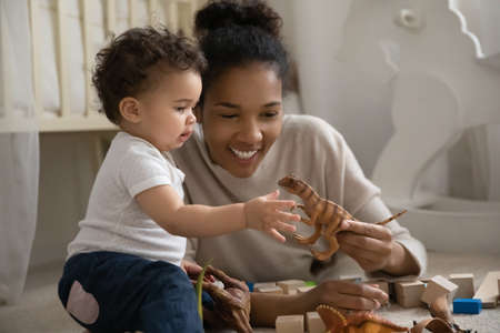 Happy young biracial mom lying on floor play with small curious ethnic baby infant at home. Smiling...