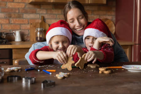Loving smiling young mom have fun baking Christmas cookies with two little children enjoy winter holidays at home. Happy mother cooking biscuits with small kids get ready for New Year celebration.の写真素材