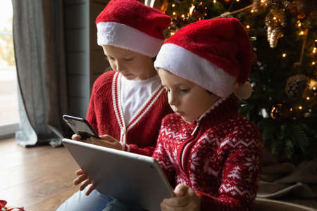 Small Caucasian boy and girl children look at gadget screens play computer online games on winter...