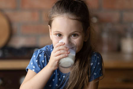 Portrait of little Caucasian girl drink tasty nutritional wholegrain milk from glass at home. Smiling small kid child enjoy delicious organic healthy lactose free yoghurt. Diet, healthcare concept.の写真素材