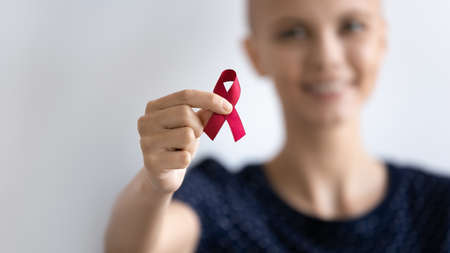 Close up smiling hairless woman holding awareness red ribbon in hand, symbol of fight, standing on white background, happy bald female supporting people with disease, regular checkup promotionの写真素材
