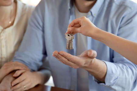 Close up shot of young spouses making deal contract and receiving keys of purchased rented leased dwelling from female real estate dealer.の写真素材