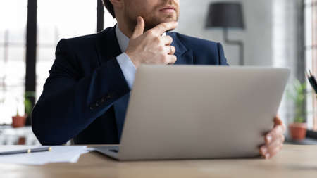 Close up pensive male ceo manager in formal suit touching chin, thinking of problem solution while...