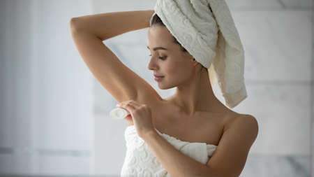 Little but important detail. Pretty millennial female wrapped in towel putting solid deodorant...