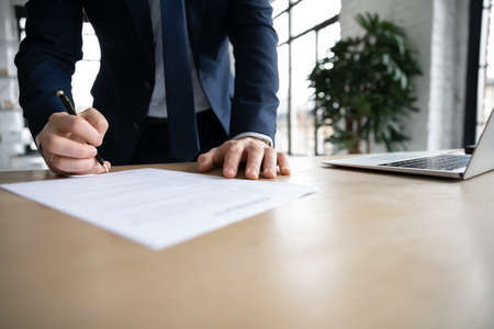 Close up young male ceo executive manager standing near table, doing company paperwork, putting...