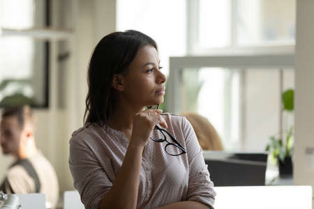 Business vision. Pensive thoughtful millennial biracial female worker employee standing at office...