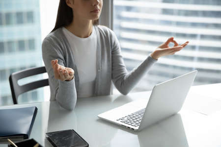 Time to meditate. Close up of calm young woman employee sitting at office table at workday practicing simple meditation resting relaxing taking pause break at work routine restoring energy balanceの写真素材
