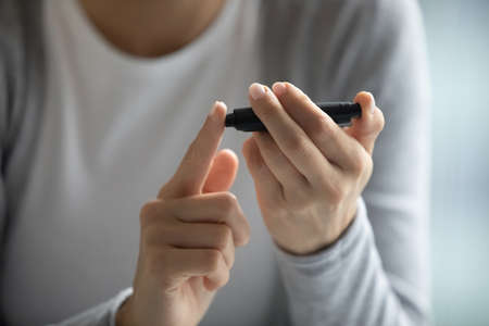 Blood glucose control. Close up of young female diabetic patient hands holding portable glucometer...