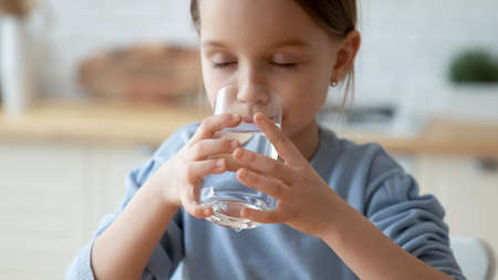 Close up dehydrated thirsty pretty little girl enjoying pure mineral water, holding glass, drinking...