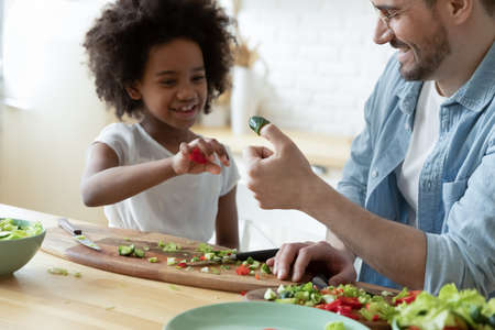 Close up happy young father and adorable African American little daughter playing with vegetables,...