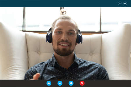 Head shot laptop display view smiling young 30s businessman in earphones working at home, holding...
