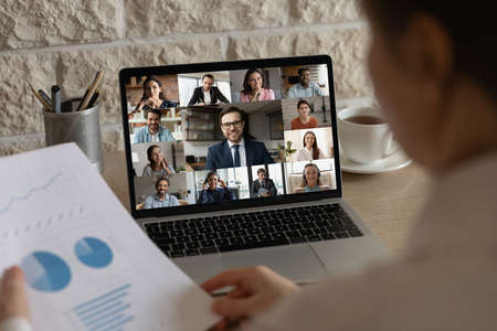 Rear back view female employee analyzing marketing research report holding video conference call brainstorming meeting with happy multiracial teammates colleagues and leader online from home.の写真素材