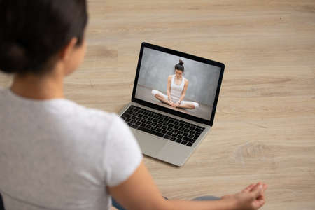 Focus on laptop screen with professional female yoga instructor sitting in lotus position, giving...