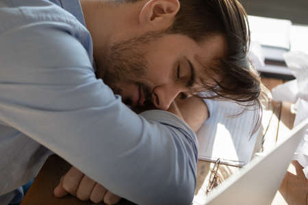 Close up business man put head on folded hands sleeping at workplace. Overloaded office employee...