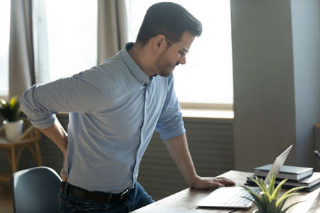Businessman touches lower back feeling pain sudden ache while get up out of office chair, muscular...