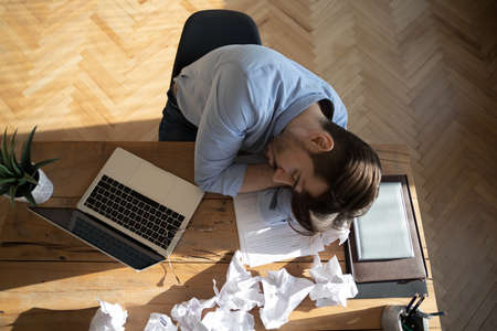 Office employee sleeping at workplace desk, above view. Desperate worker not find solution or...