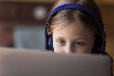 Teleeducation. Close up of attentive schoolgirl in headphones looking at laptop screen learning...