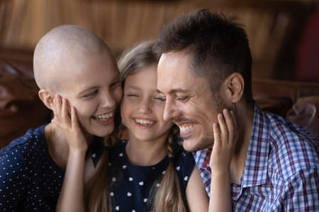 I love you, mommy and daddy. Happy smiling little girl daughter sitting on sofa at home embracing...
