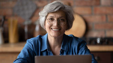 Head shot portrait smiling mature woman wearing glasses using laptop, teacher mentor working online...