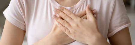 With all my soul. Close up banner image of unknown young female palms folded on chest close to heart...