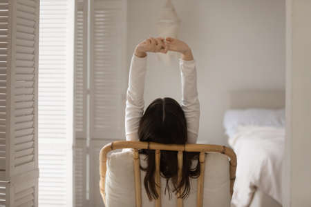 Meeting morning. Back rear view of peaceful relaxed young woman sitting in cozy wicker armchair at...