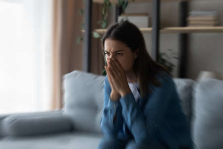 Pensive upset young Caucasian woman sit on sofa at home look in distance morning or yearning....