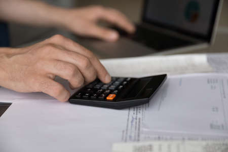 Crop close up of man count household expenses expenditures on calculator paying bills taxes on...