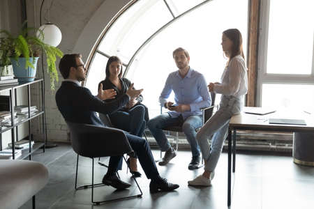 Concentrated millennial male ceo leader setting targets to staff workforce members on daily briefing in modern office, young business partners colleagues sitting in circle planning teamwork on meetingの写真素材