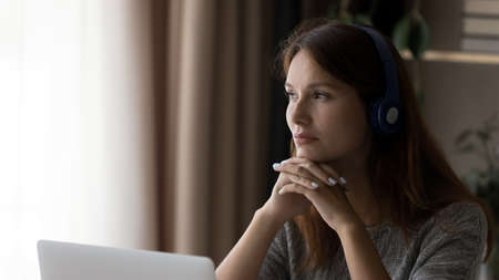 Distracted dreamy young woman in headphones looking away in distance, thinking of problem solution,...