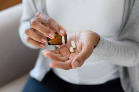 Crop close up of African American woman take pills or tablets from bottle. Biracial female have nutritional dietary supplements or medicines from packaging. Healthcare, pharmacy, wellness concept.の写真素材