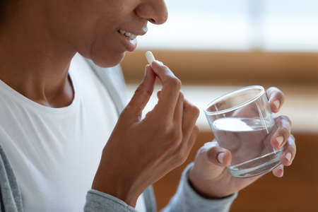 Crop close up of smiling young African American woman take daily dose of vitamin or dietary supplements. Millennial biracial female have medicines or pills drugs at home. Healthcare concept.の写真素材