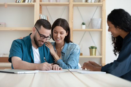 Happy young Caucasian couple put signature on document close deal with female realtor or broker at...