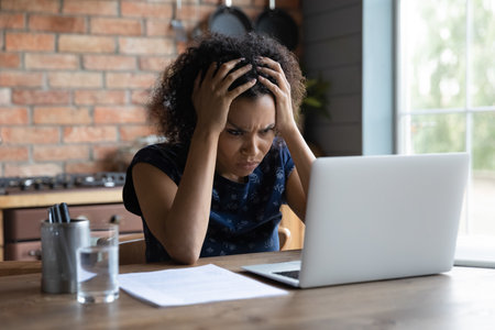 Confused young african ethnicity woman looking at computer screen, feeling stressed of reading bad news, getting dismissal notice by email, bank loan rejection notification, unlucky people concept.の写真素材