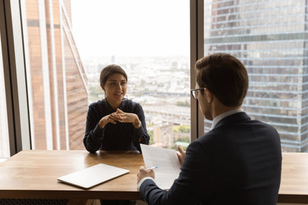 Young Indian female job applicant talk with male employer at company interview in office. Back view of businessman have recruitment meeting with ethnic woman employee. Employment concept.の写真素材