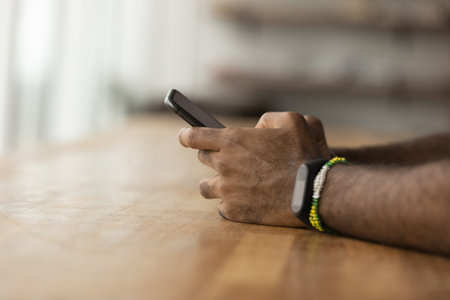 Crop close up of African American man sit at desk use modern smartphone gadget. Biracial male...