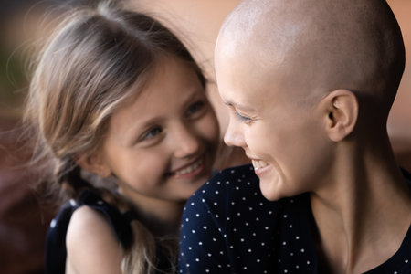 Close up happy cancer patient sick mother and little daughter hugging, laughing, enjoying tender moment together, cuddling, adorable child supporting mum suffering from oncology, expressing loveの写真素材