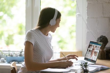 Close up young woman wearing headphones studying online with mature teacher, using laptop, female...