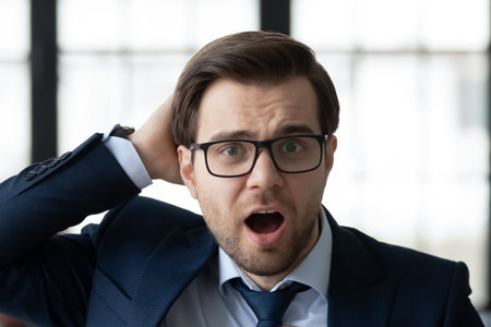 Head shot shocked businessman wearing glasses looking at camera, standing in office, employee with open mouth amazed by unbelievable news, unexpected money problem, bankruptcy notificationの写真素材