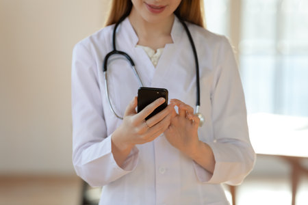 Crop close up of woman doctor in white medical uniform hold use smartphone consulting client online. Female nurse or GP look at cellphone screen, have webcam video call or consultation with patient.の写真素材