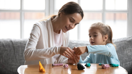 Caring young mother making plasticine figures with little baby daughter, developing creativity at home. Affectionate nanny helping small girl, involved in handmade activity indoors, daycare concept.の写真素材
