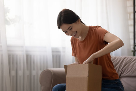 Pleasant surprise delivered by mail. Curious young woman shopper unpacking cardboard box getting order from online store. Happy excited millennial lady opening postal parcel amazed with gift receivedの写真素材