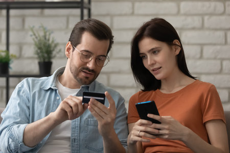 Believe me, it is easy. Confident husband teaching interested young wife to make cashless payment using mobile banking app. Millennial male explaining female how to enter plastic card details onlineの写真素材